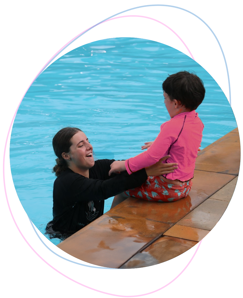 Nereids swim teacher in the water gently encouraging a hesitant child at the pool’s edge during a one-on-one lesson