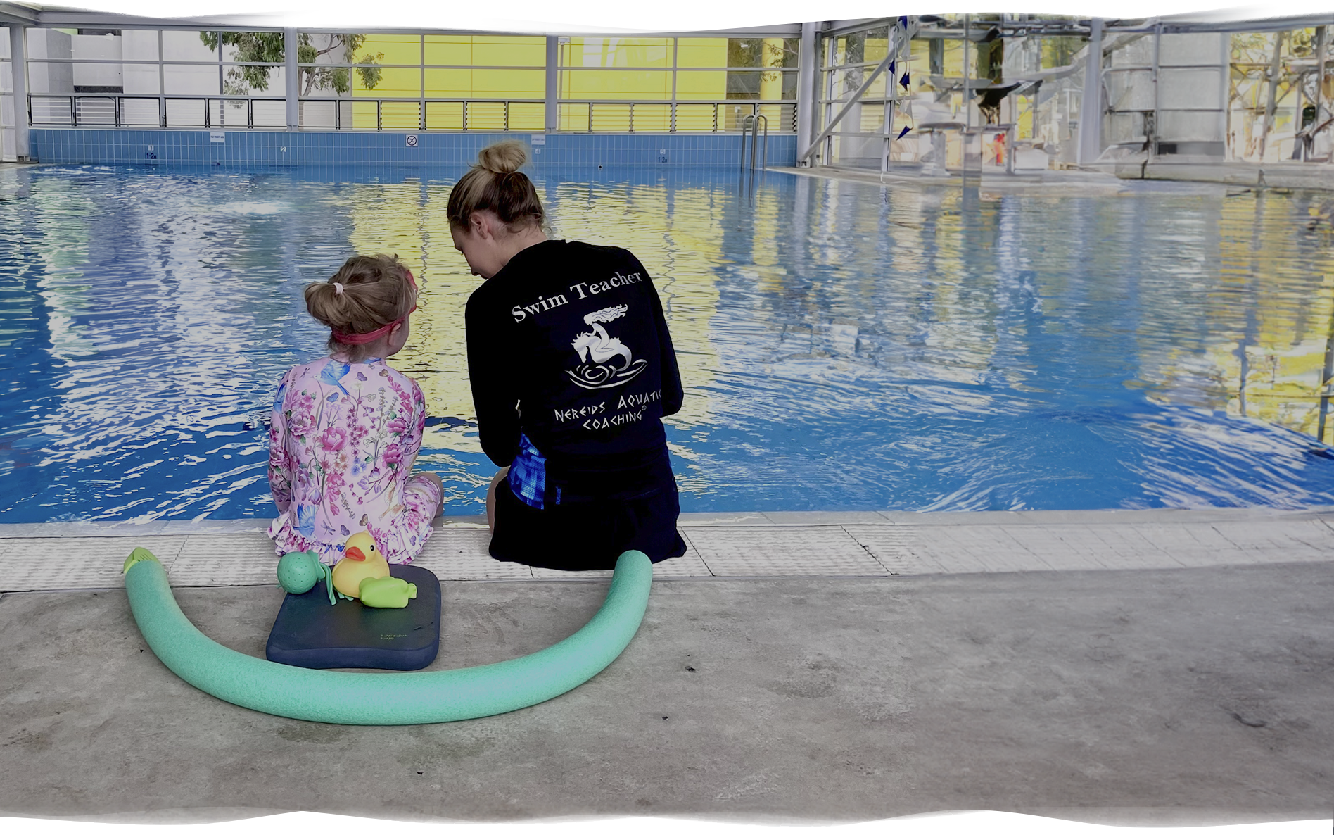 Nereids swim teacher sitting beside a nervous child near the pool, gently guiding them before a lesson.