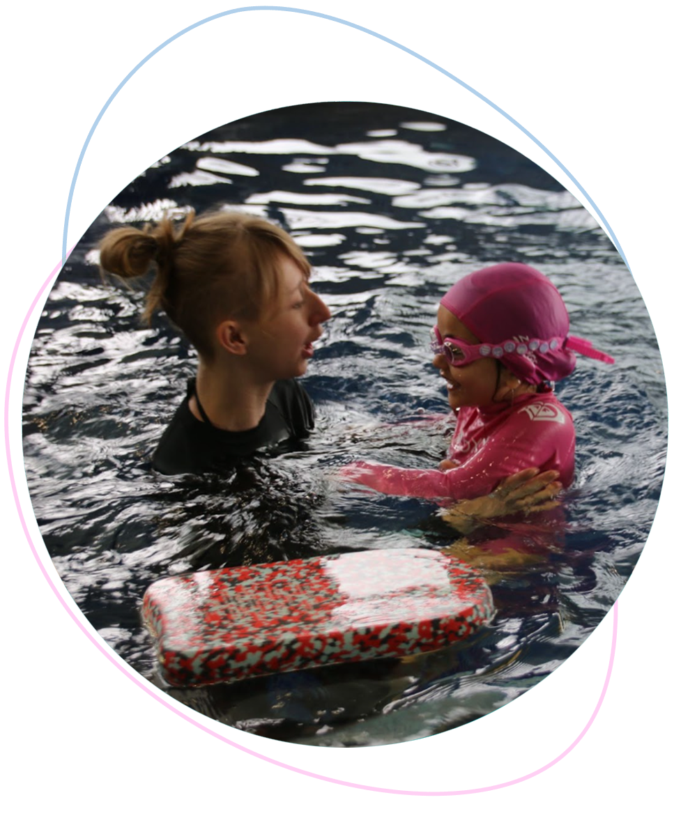 Nereids swim teacher gently supporting a young girl by holding under her arms while they face each other above the water during a private swimming lesson