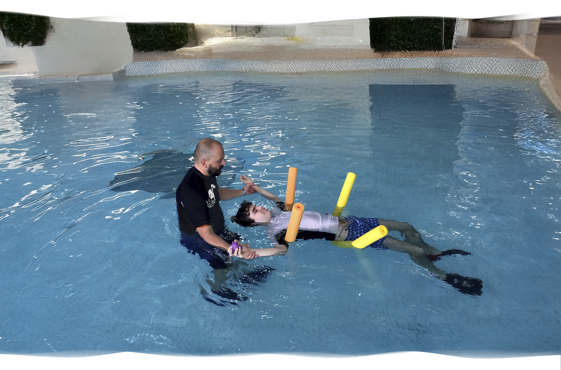 Nereids swim teacher supporting an autistic student gently floating on his back using pool noodles, creating a calm and safe environment.