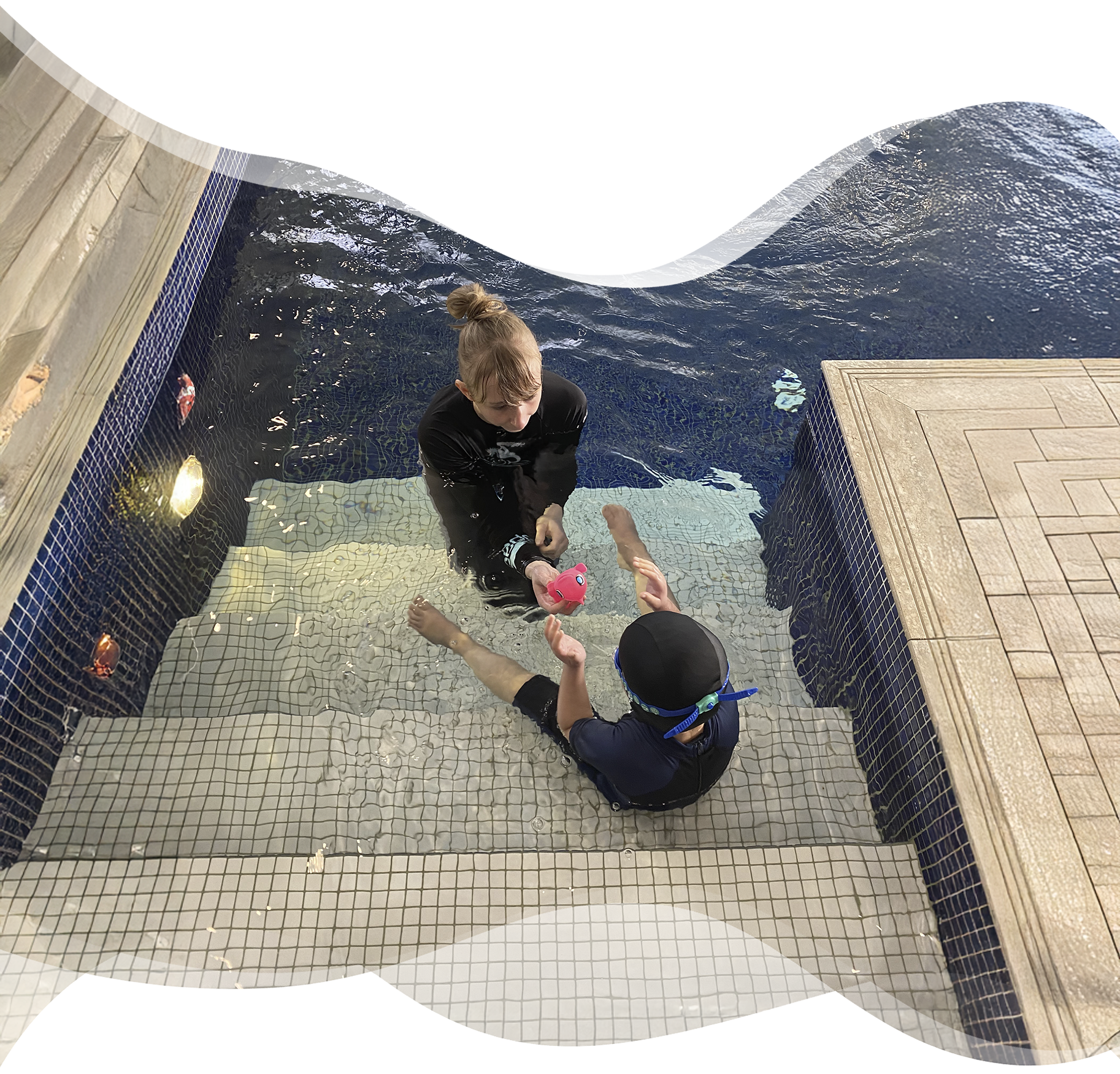 Nereids swim teacher engaging a young child with disabilities at the poolside steps using a playful toy, fostering trust and emotional safety.