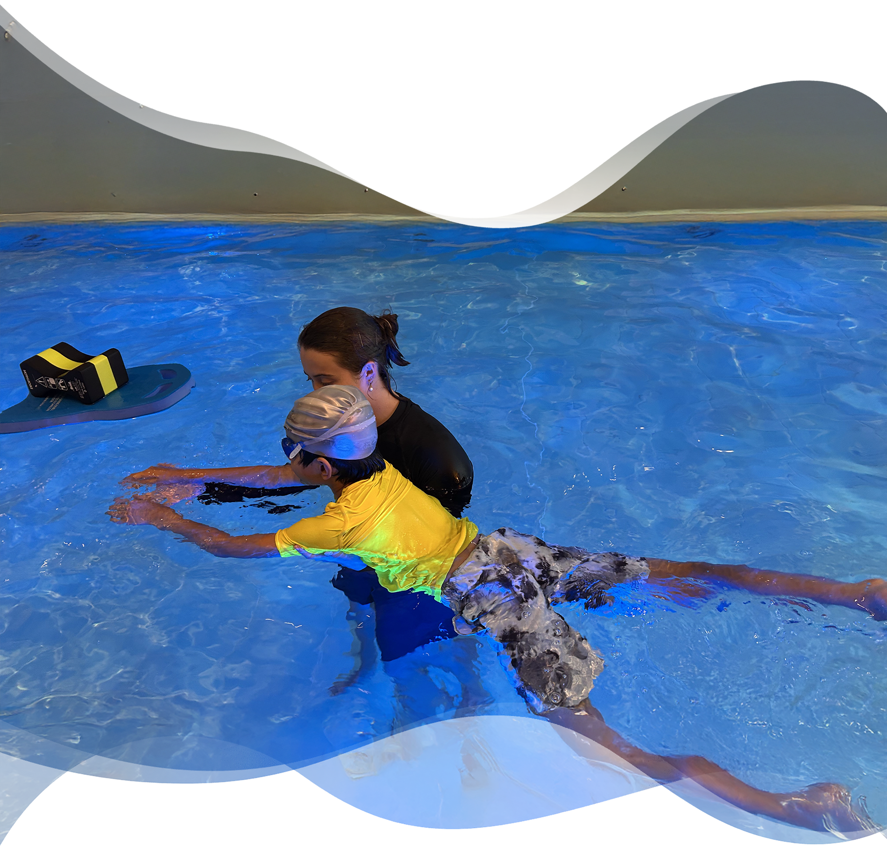 Nereids swim teacher gently assisting a child in a bright yellow rash shirt to stretch and float in the water, encouraging freedom of movement.