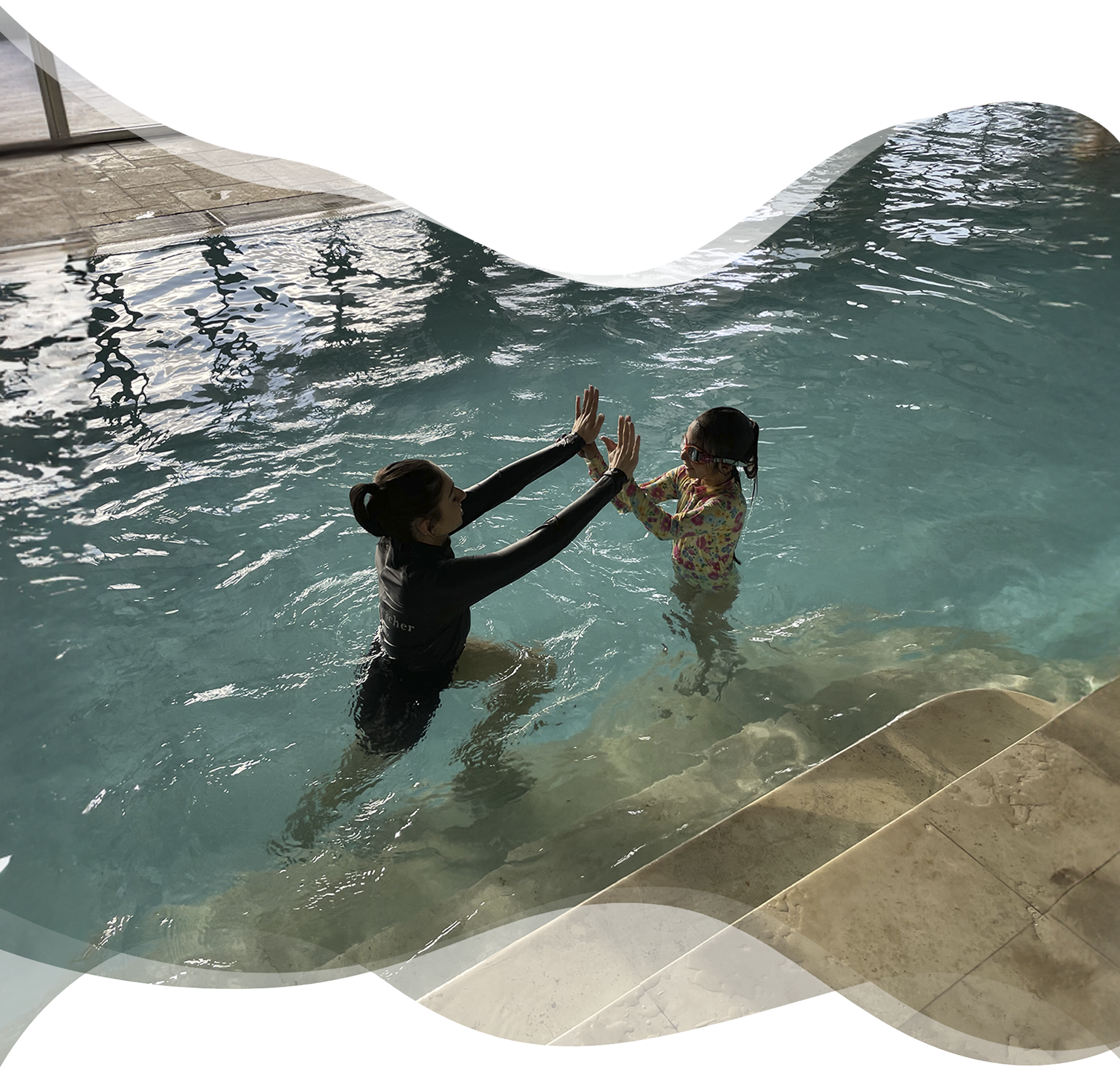 A joyful moment between student and Nereids teacher as they high-five in the pool — celebrating progress, connection, and the joy of learning together.