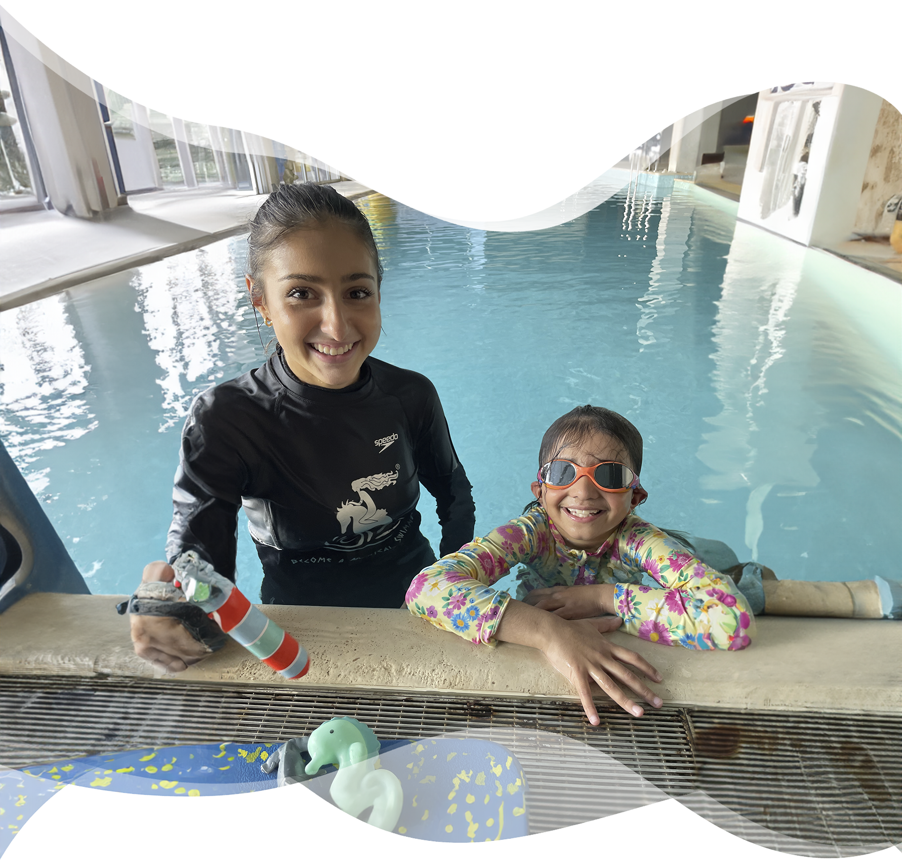 A happy young swimmer stands poolside next to her Nereids teacher, both smiling proudly after a lesson — a moment of trust, connection, and joy.