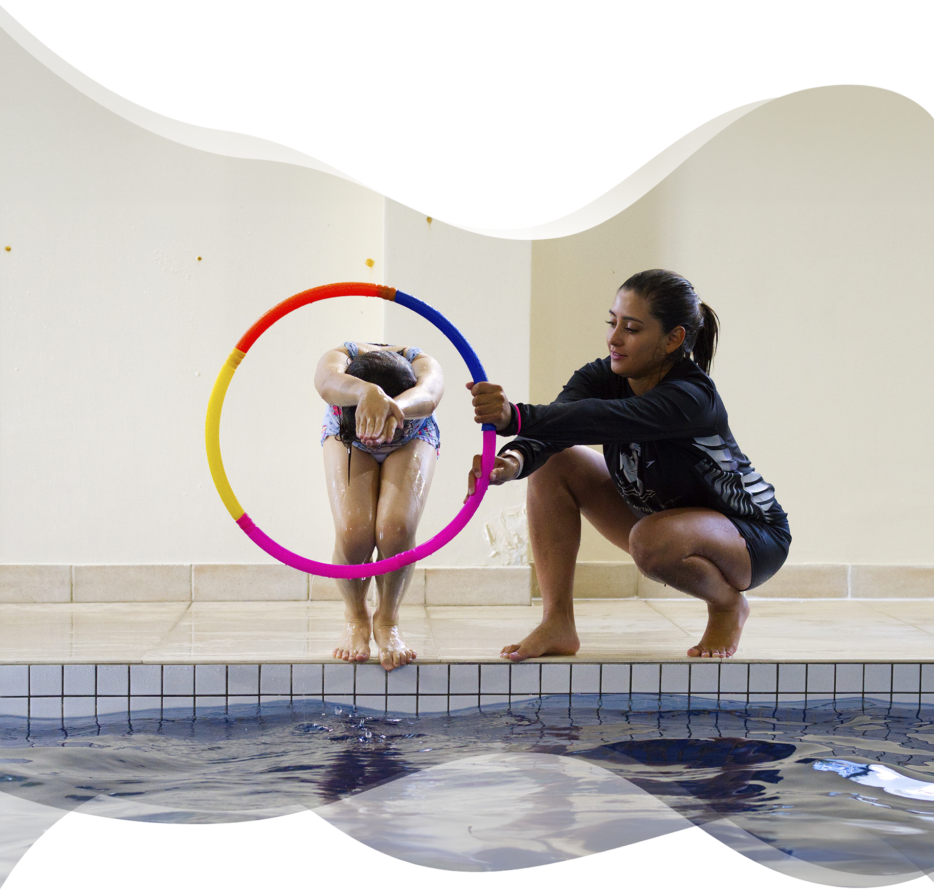 A confident young swimmer prepares to dive through a floating hoop, guided by a Nereids swim teacher — combining skill development with play, courage, and coordination.