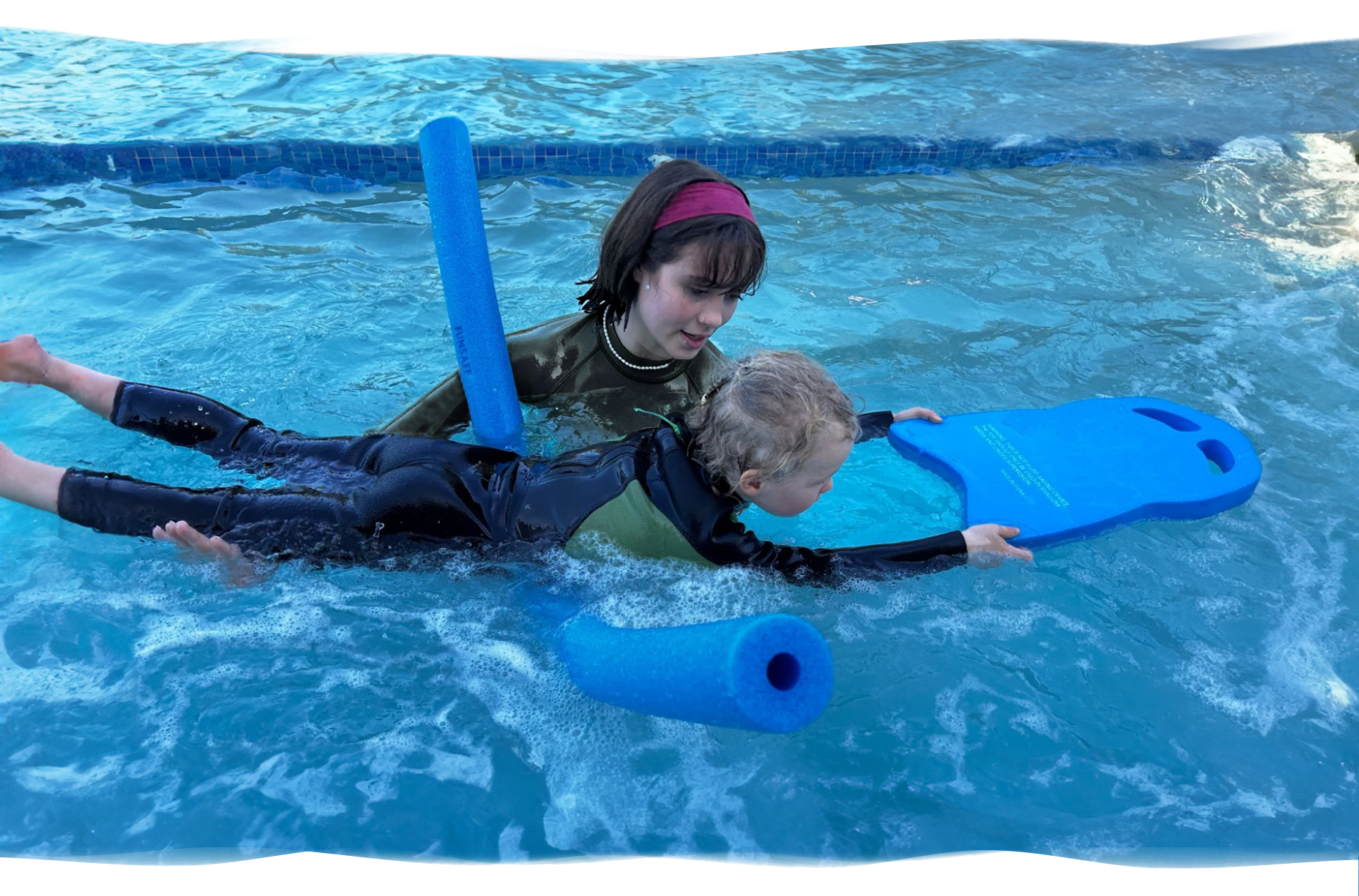 Nereids swim teacher gently supporting a preschool boy using pool noodles as he learns to float, showing trust, encouragement, and early swimming confidence.