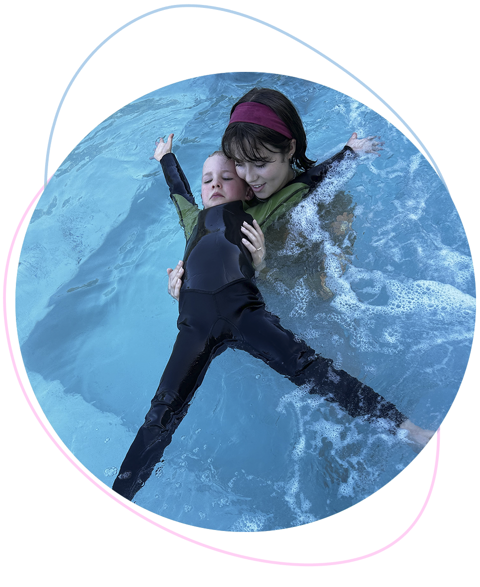 Preschool boy attempting a starfish float with gentle support from a Nereids swim teacher behind him, capturing the early stages of confidence and calm in the water.