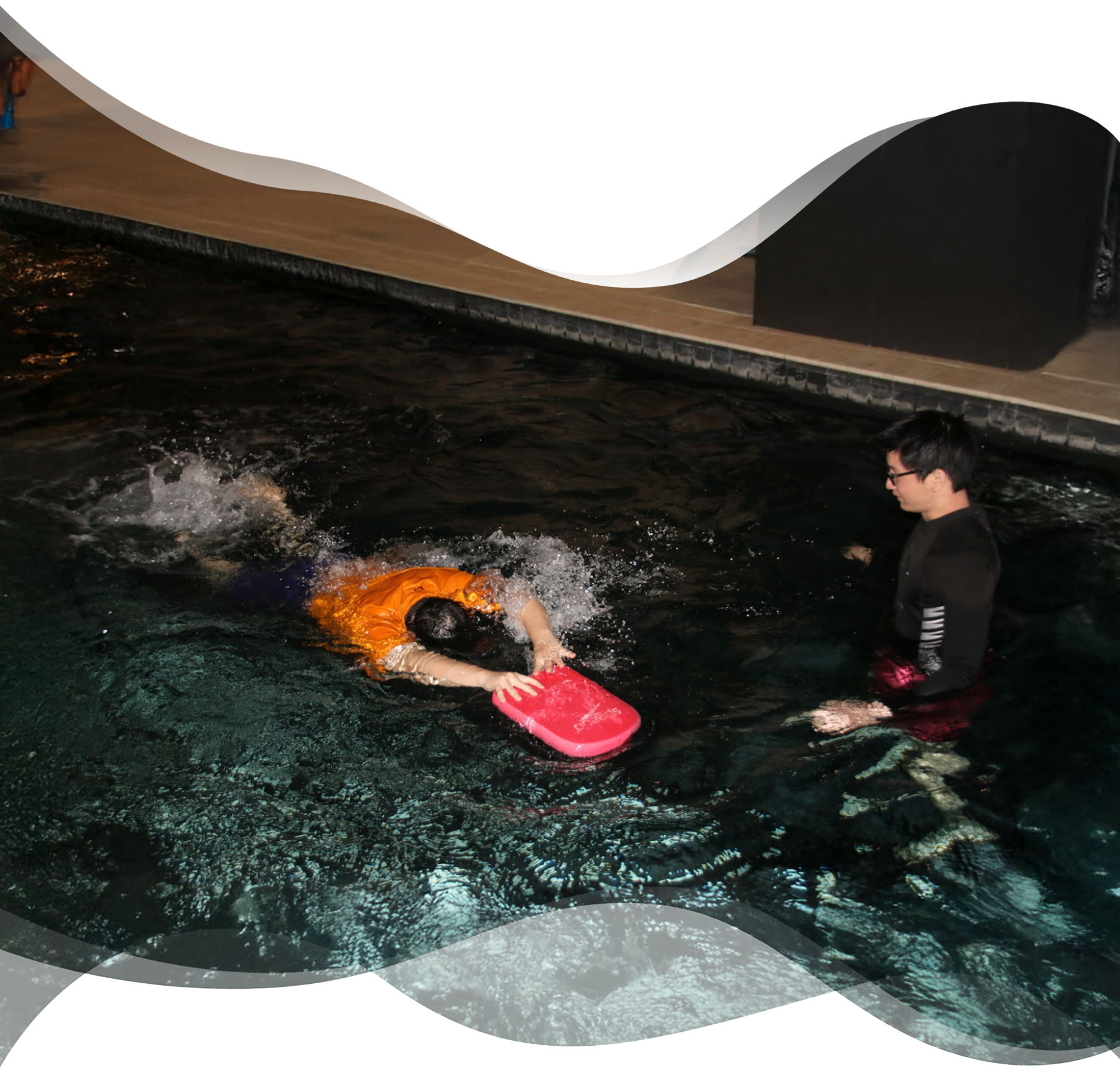 Adult beginner kicking freestyle with kickboard while Nereids swim teacher observes proudly nearby