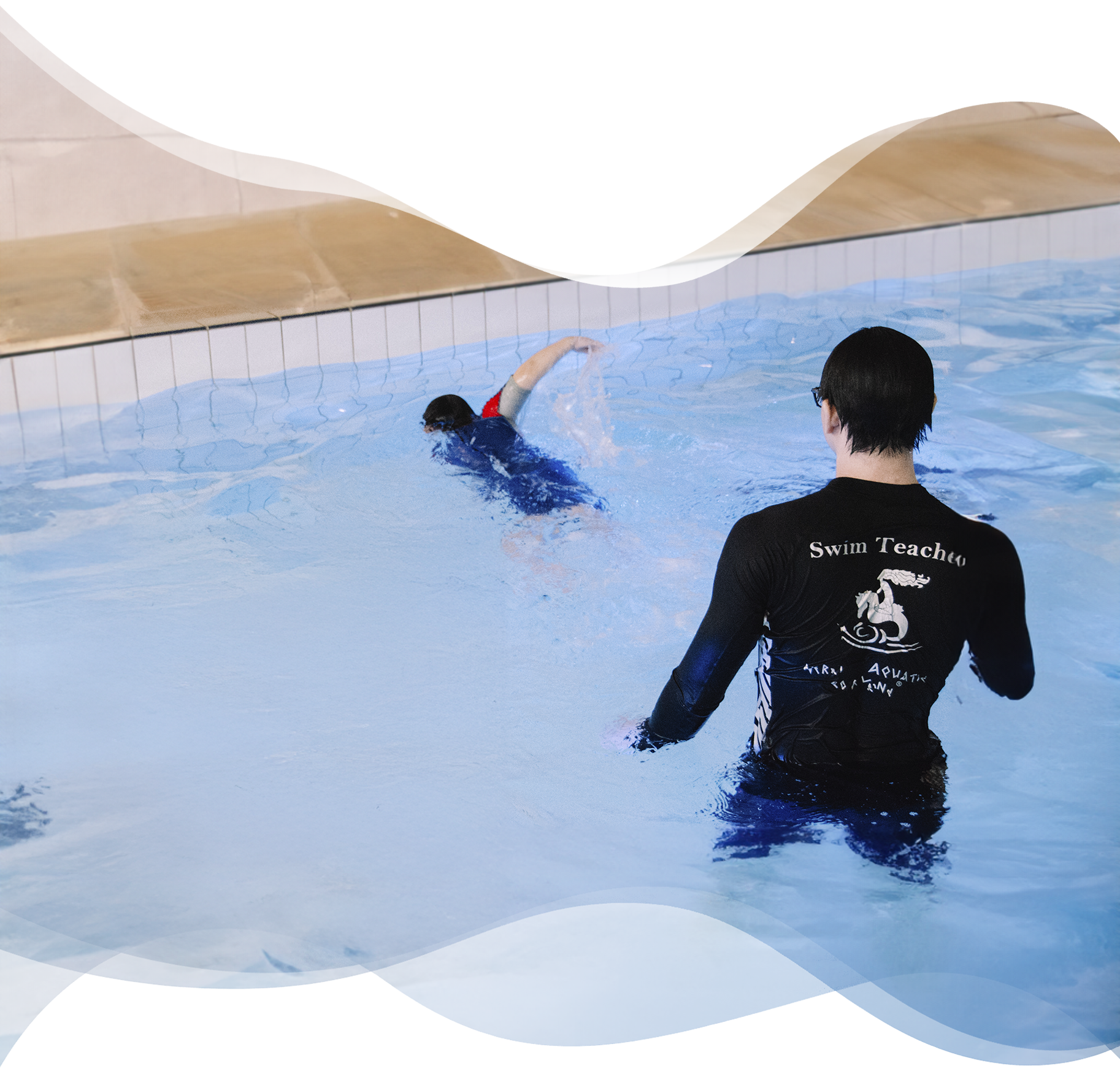 A Nereids swim teacher stands behind a boy practicing freestyle, observing his form closely to refine stroke efficiency and control
