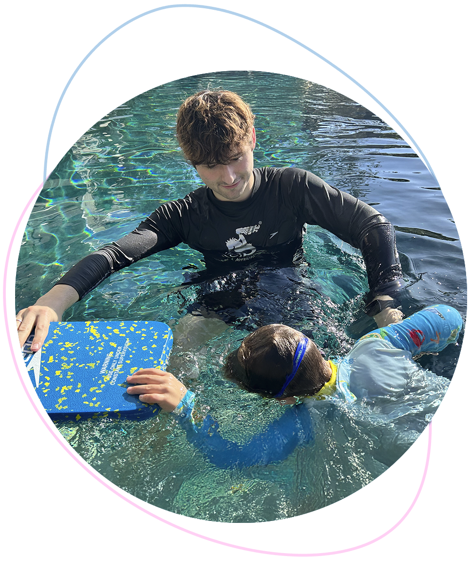 Nereids swim teacher gently guides a school-age boy in breathing drills using a kickboard, focusing on rhythm, body control, and calm presence.