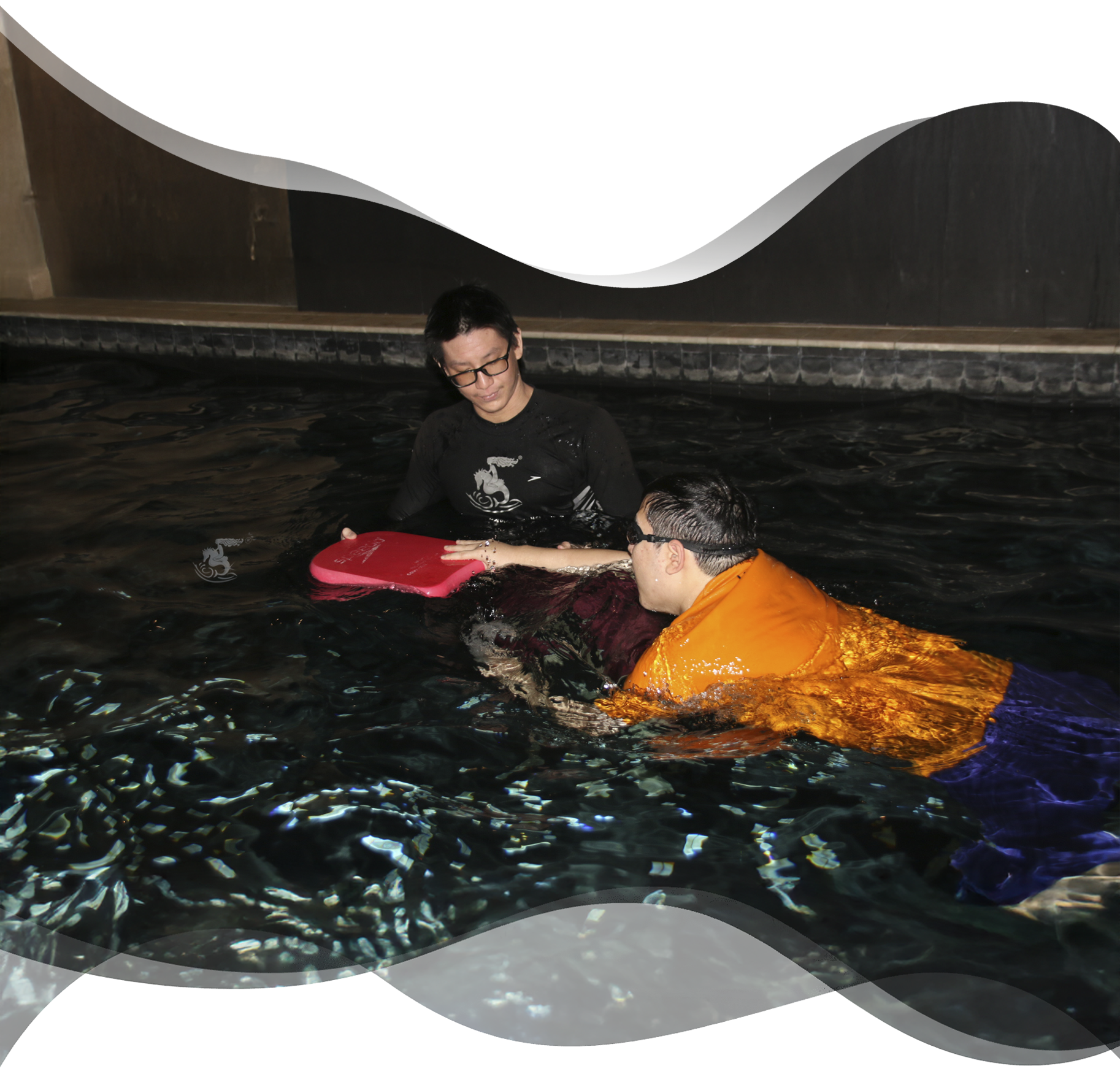 Nereids swim teacher beside adult swimmer preparing for kickboard drill with focus and guidance