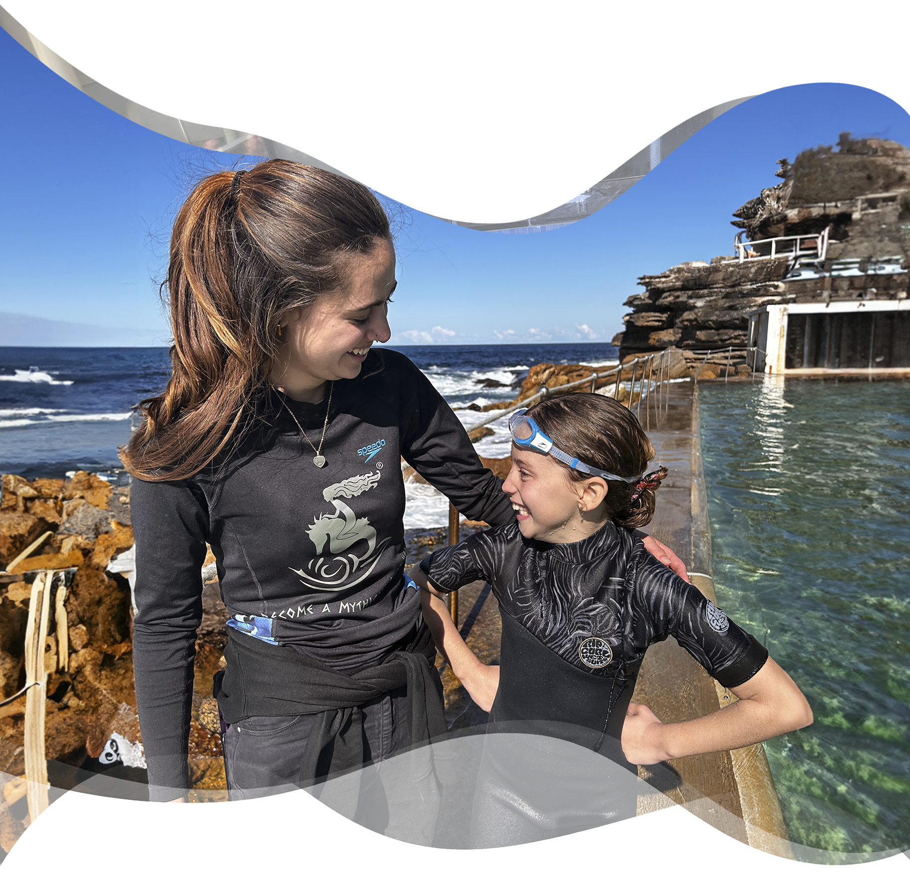 A happy young girl stands beside her Nereids swim teacher after a private swimming lesson, both relaxed and joyful — showing the bond and confidence built through the Triton program.
